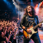 Artista tocando guitarra eléctrica en directo frente a una multitud.